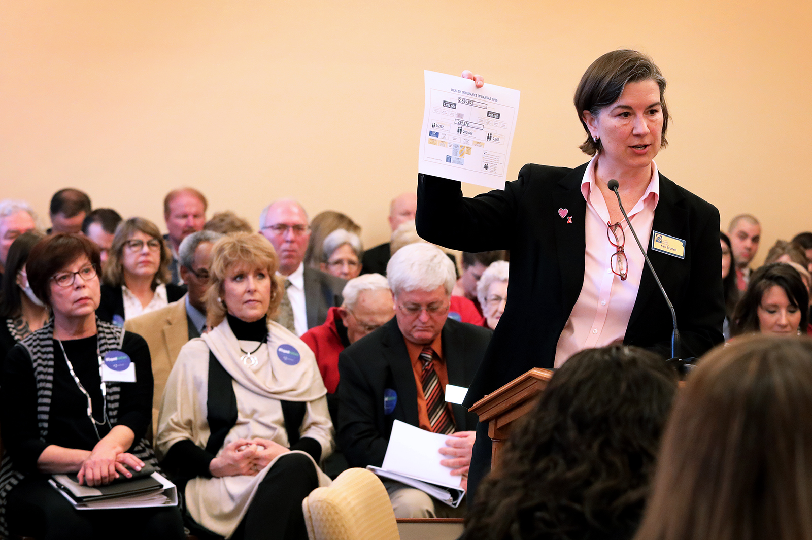 Kari Bruffett holds up a document while testifying before a seated audience